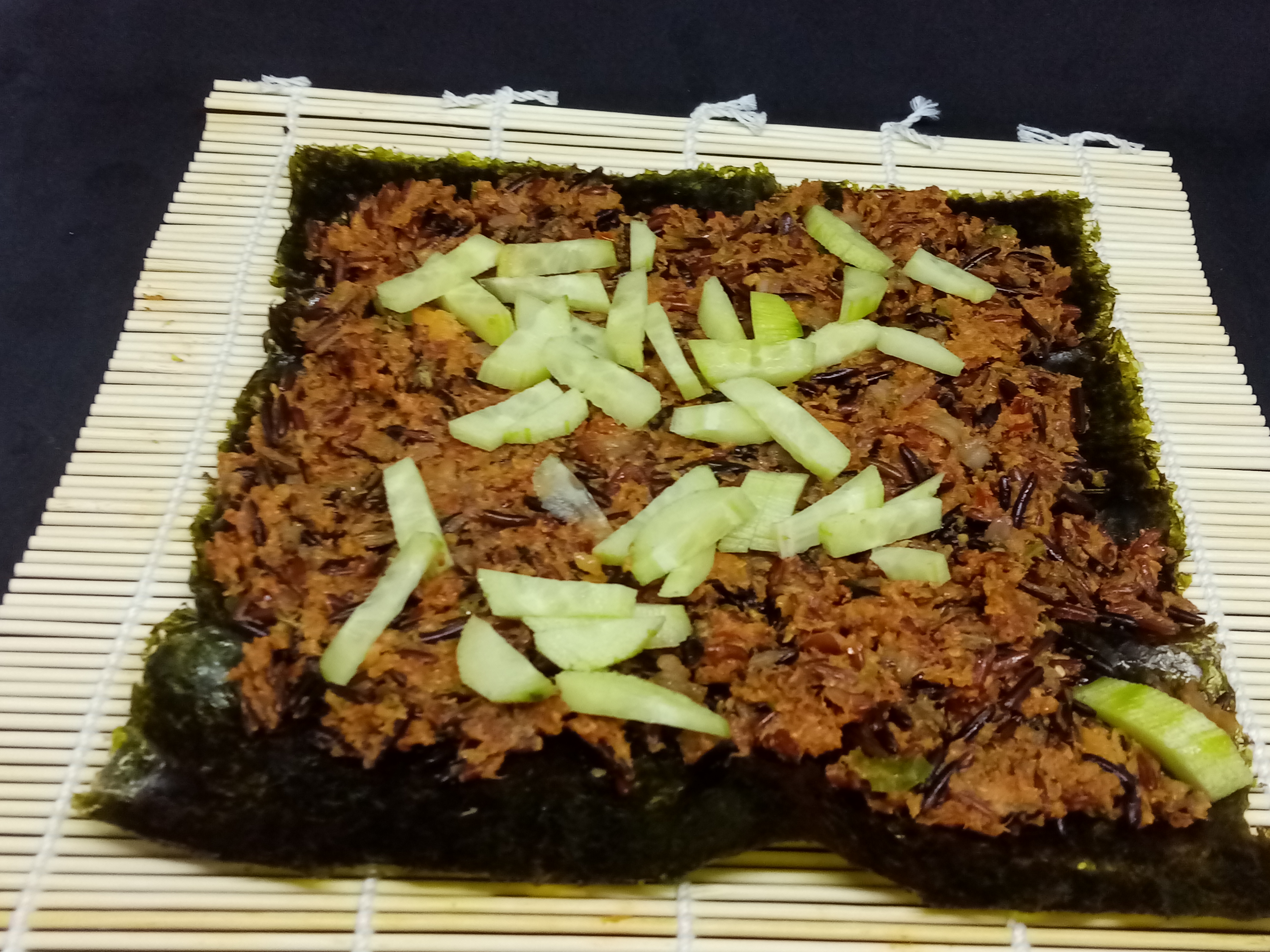 rice and sliced cucumber on a nori sheet on a bamboo mat